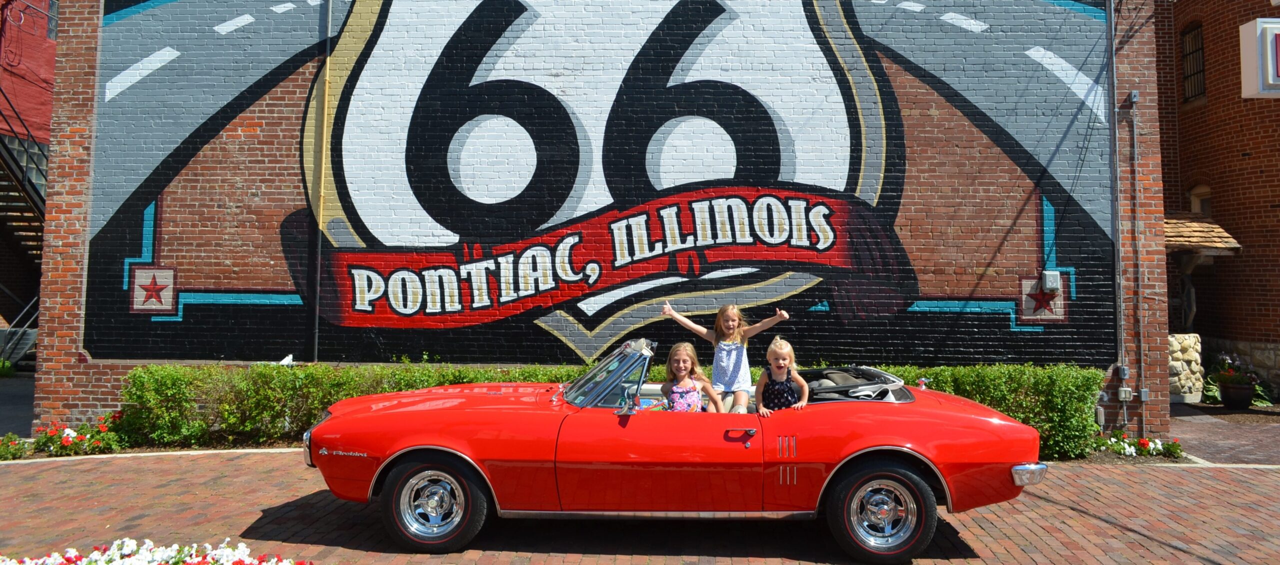 Children in a vintage convertible in front of the Pontiac, IL Route 66 mural